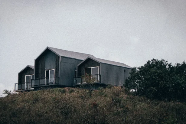 Contemporary cabin perched on a hillside in a cloudy, rural setting.