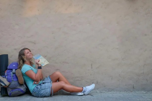 Smiling female traveler sitting by a wall with a map, enjoying a moment of relaxation on her journey.
