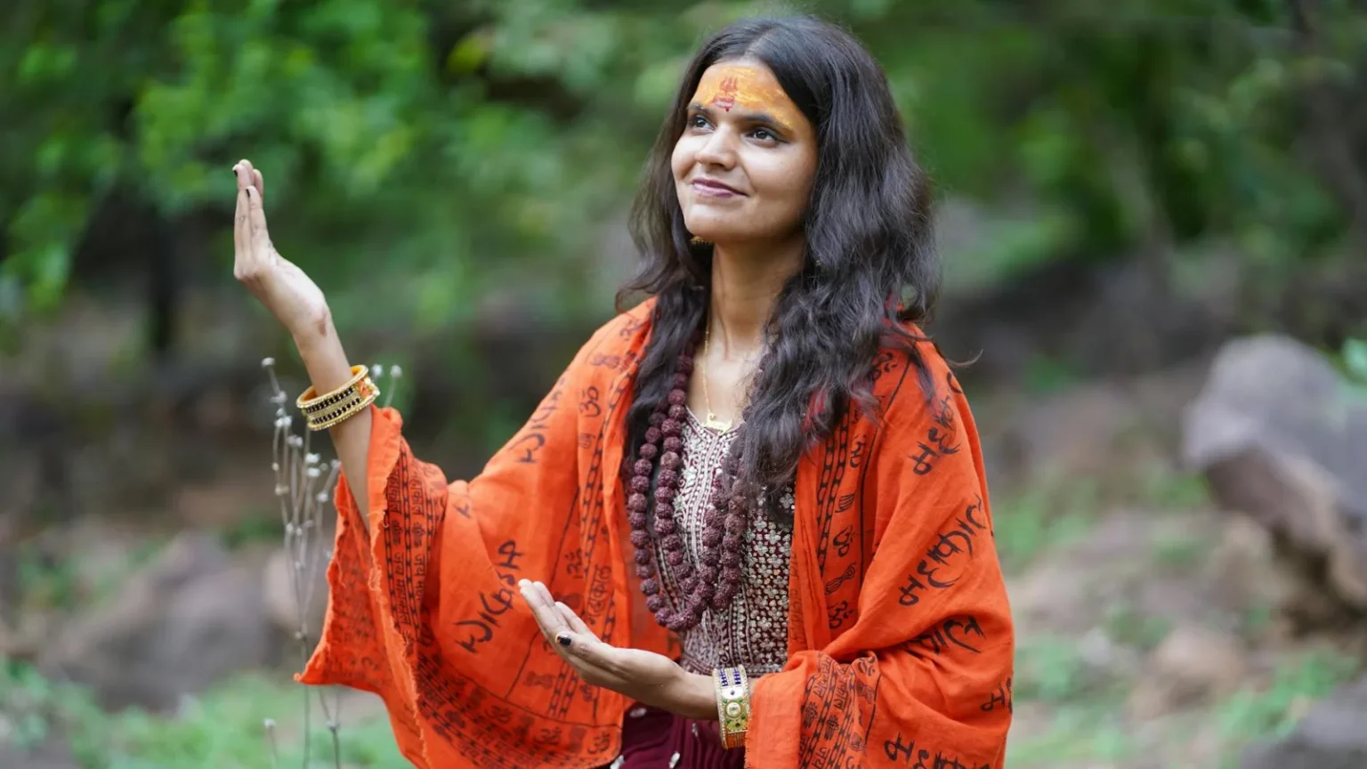 A woman in traditional attire meditating peacefully in a natural setting.