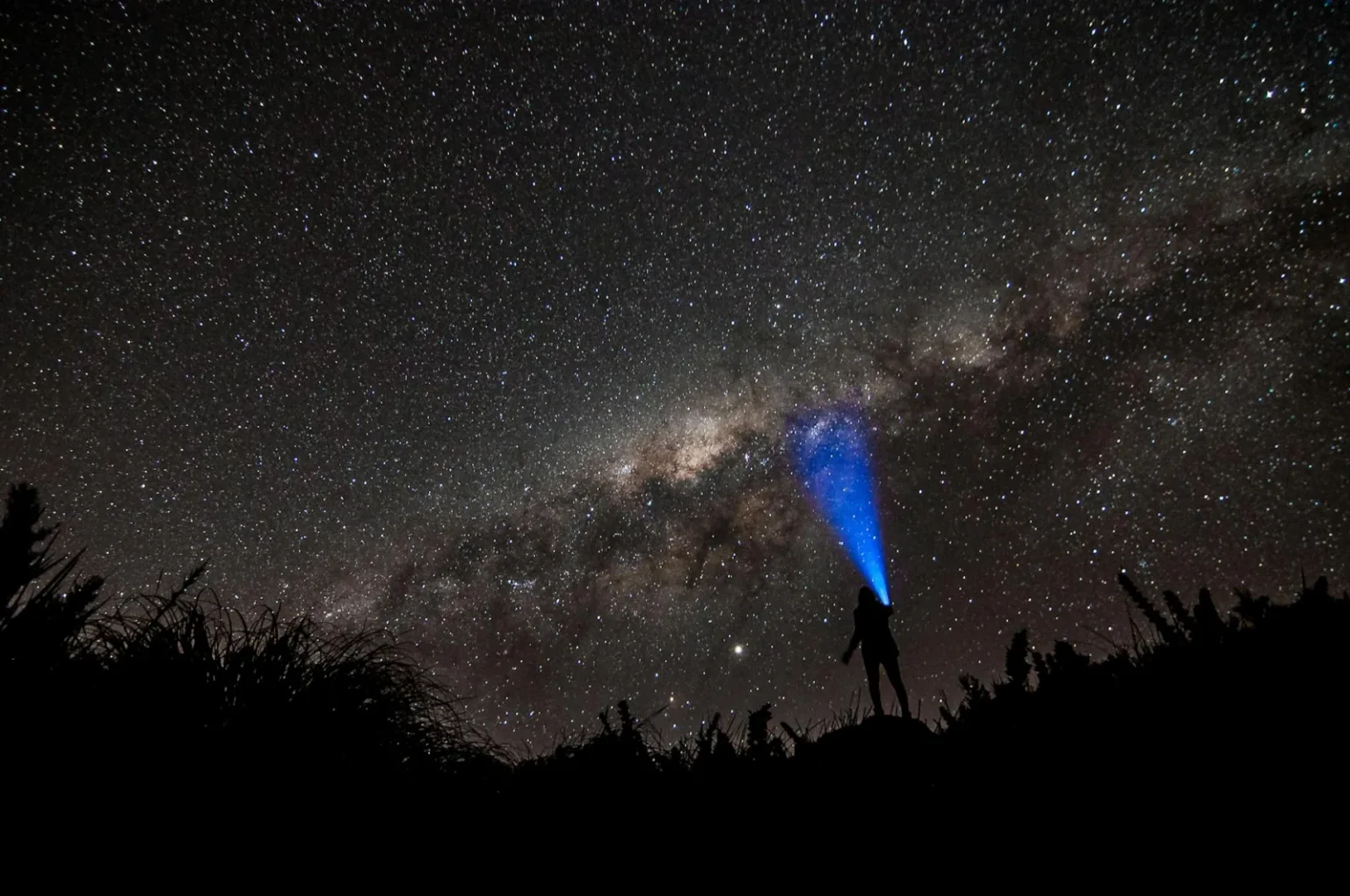 Person with flashlight under the starlit sky of the Milky Way galaxy at night.