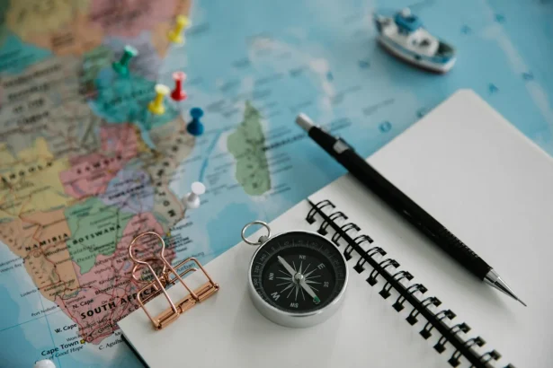 Flat lay of travel planning tools including a map, compass, notebook, and pen.