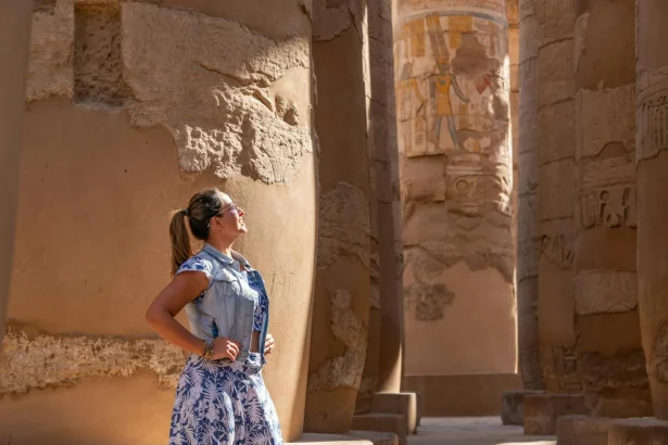Woman in Luxor Temple admiring ancient carved columns in sunlight.