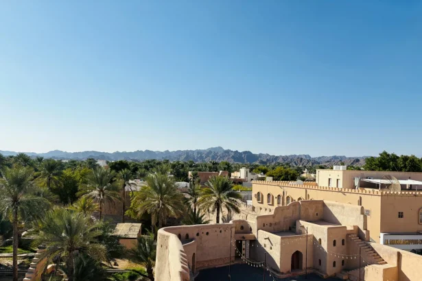 View of Nizwa Fort and the surrounding oasis against Hajar Mountains under a clear blue sky.