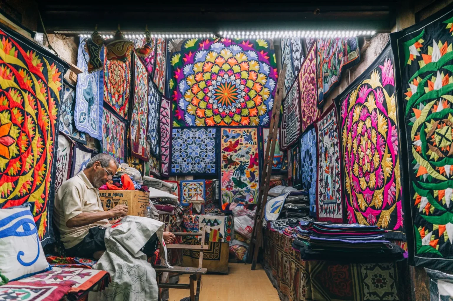 Colorful traditional quilts displayed in a shop in Cairo with a craftsman working.