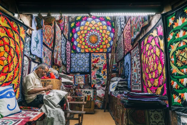 Colorful traditional quilts displayed in a shop in Cairo with a craftsman working.