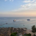Stunning aerial view of Sharm El Sheikh's beach and sea during sunset with boats and parasols.