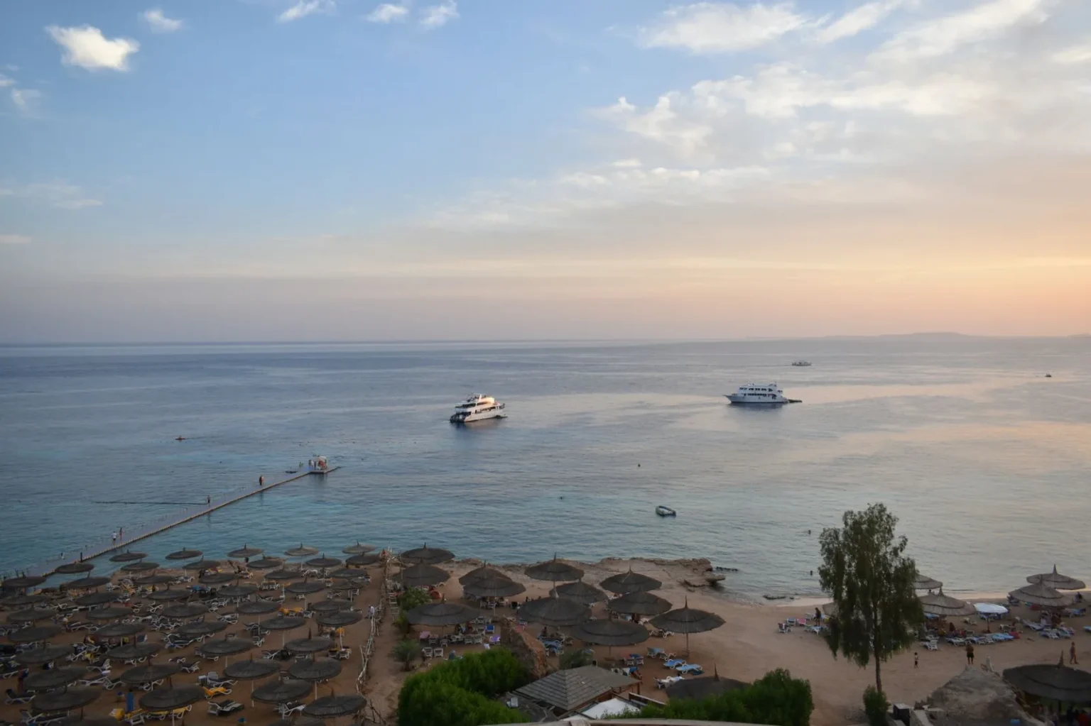 Stunning aerial view of Sharm El Sheikh's beach and sea during sunset with boats and parasols.