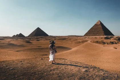 A woman stands in the Egyptian desert, with pyramids in the background.