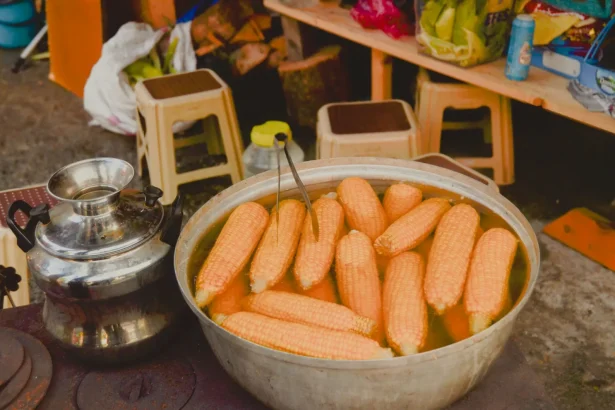 Close up of boiled corn on the cob in a large pot at an outdoor street market.
