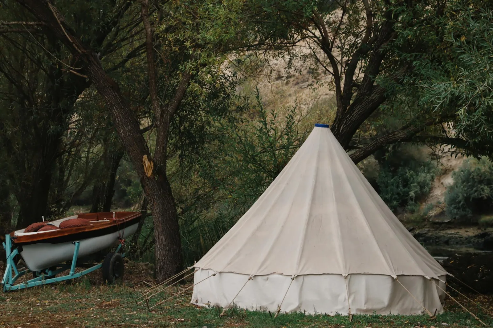 Rustic camping scene with a tent and a boat in a tranquil forest setting.