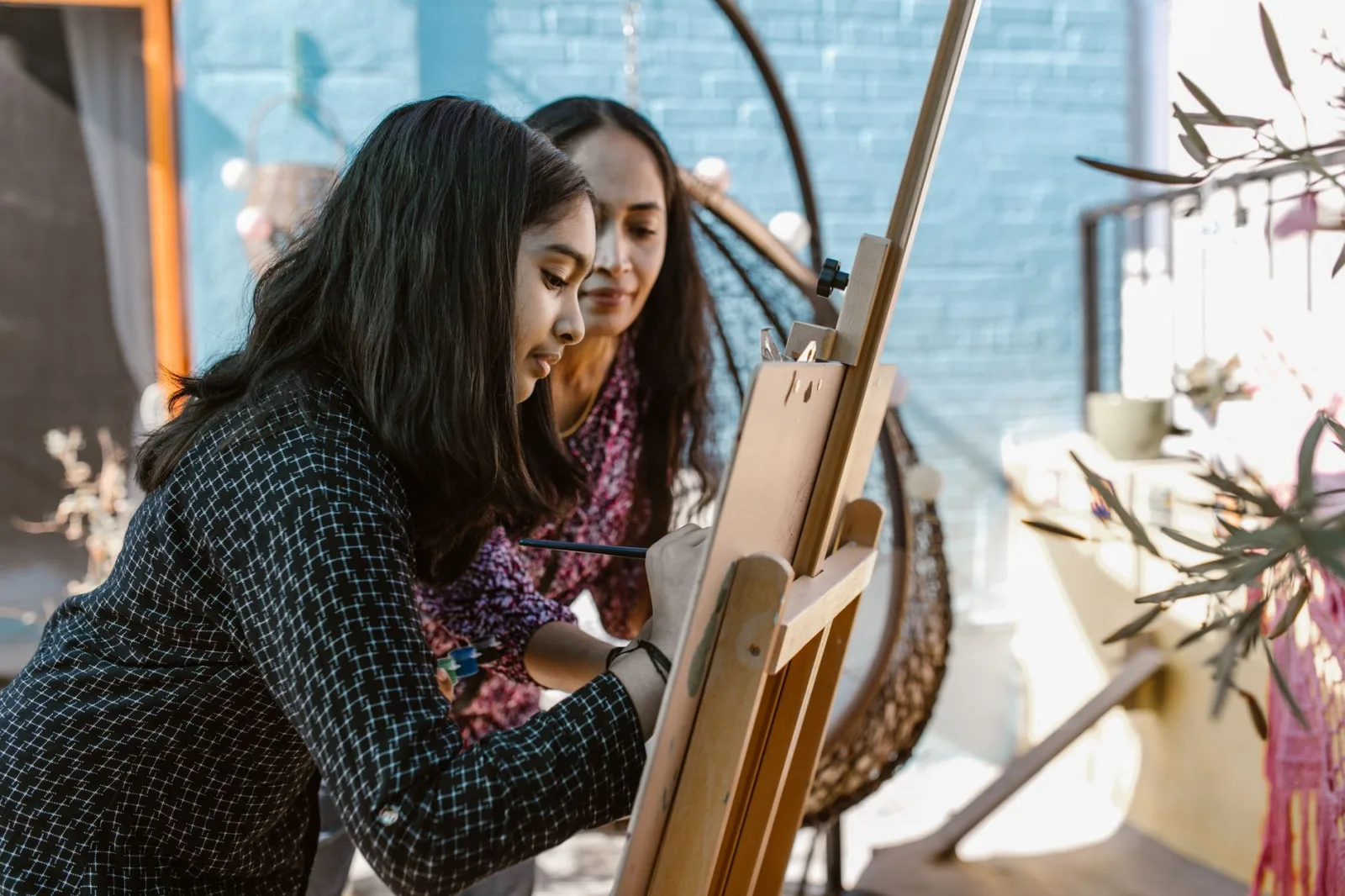A woman and her daughter bond through painting outdoors on a sunny day.