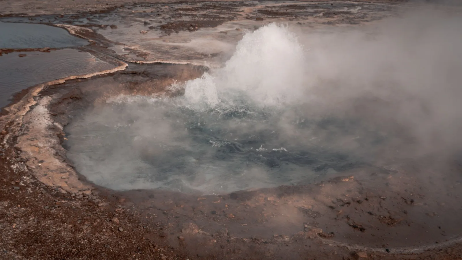 An active geyser erupting in the Icelandic landscape, captured in vivid detail.