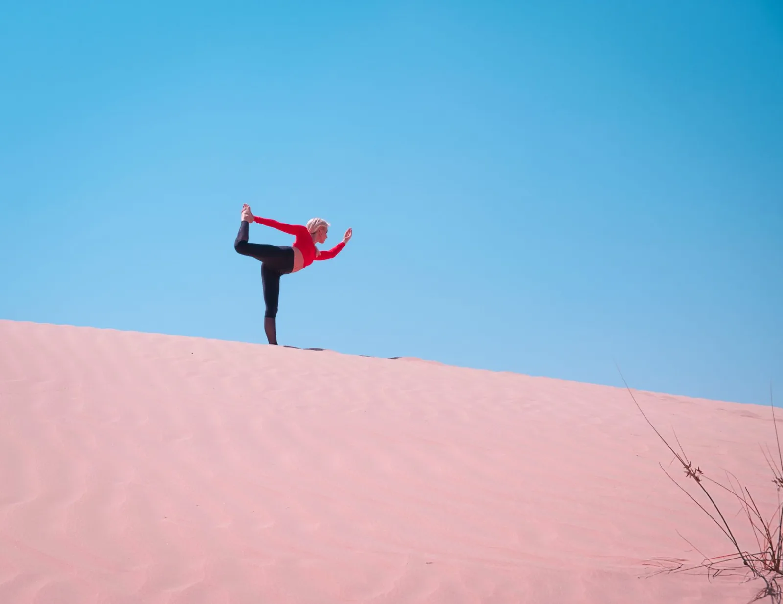 A woman practices yoga on sand dunes in Dubai, enjoying the clear blue sky and vast desert landscape.