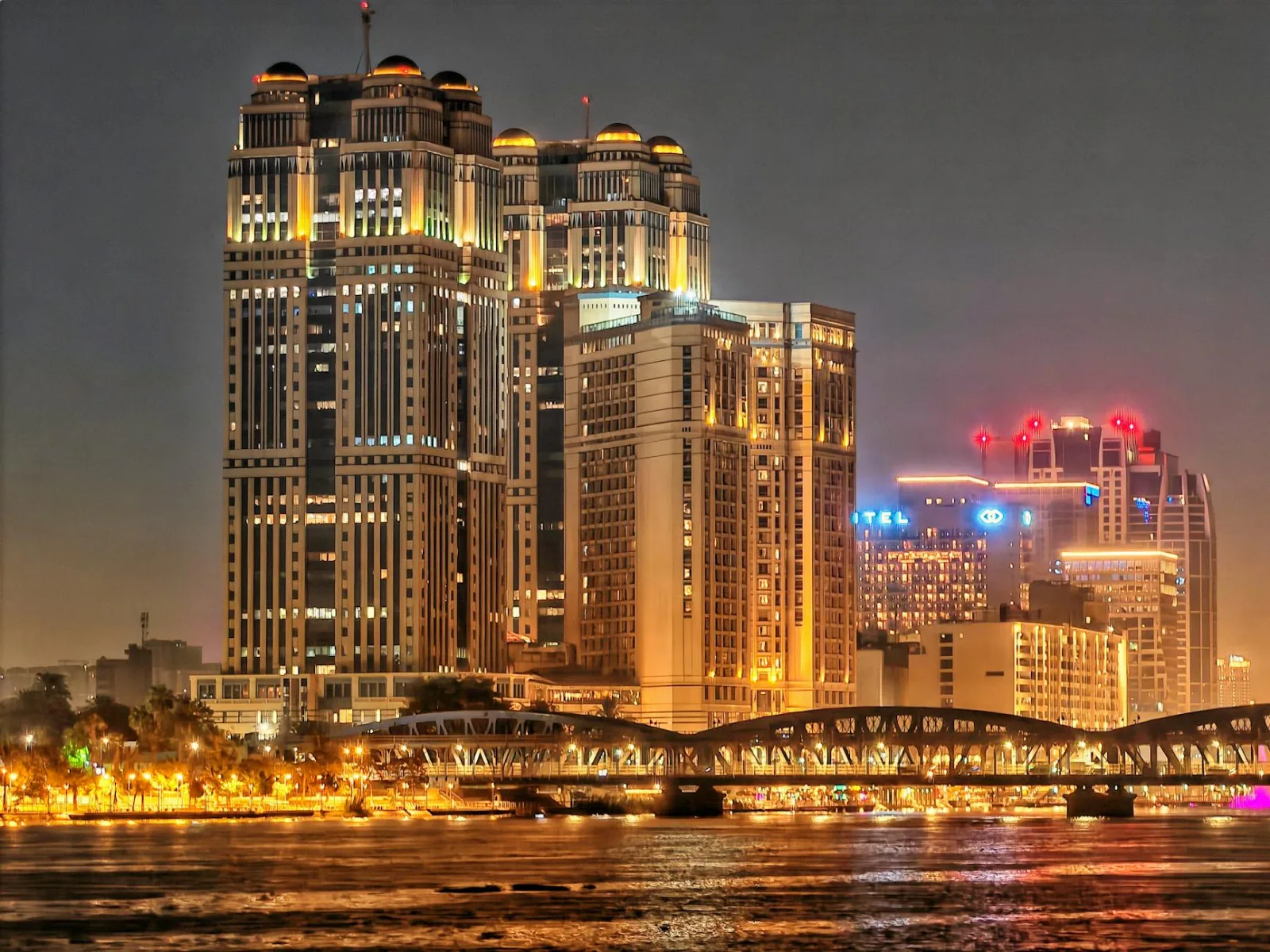 Stunning night view of illuminated skyscrapers and a bridge reflecting on the river.
