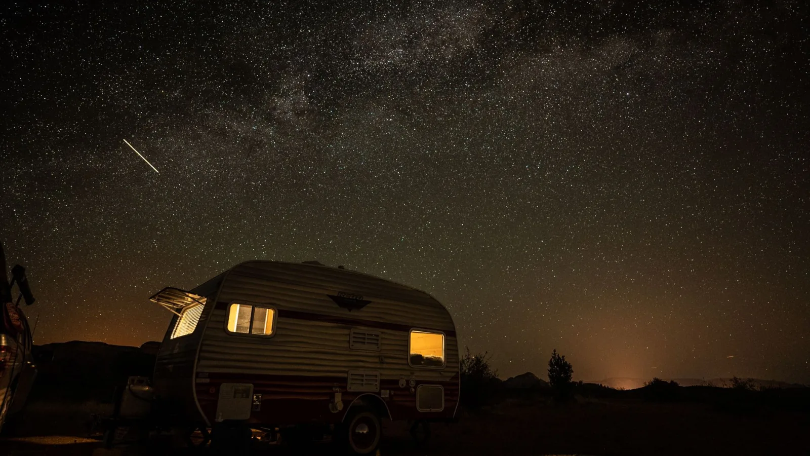 A serene night scene with a vintage camper under a starry sky and shooting star.