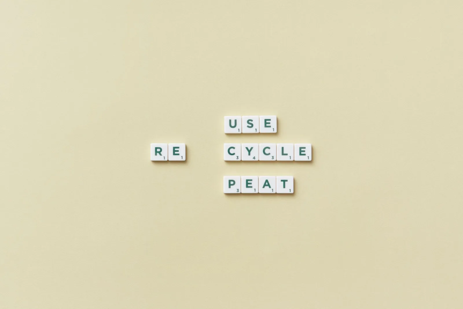 Letter tiles spelling 'reuse recycle repeat' on a simple background, promoting sustainability.