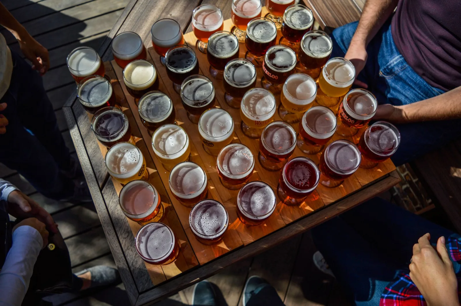 From above of crop anonymous group of friends relaxing in cafe at wooden table with many glasses of various types of beer