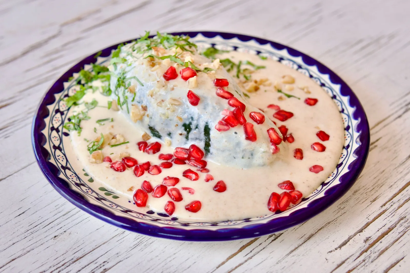 Delicious Chiles en Nogada dish garnished with pomegranate seeds and cream sauce, served on a decorative plate.
