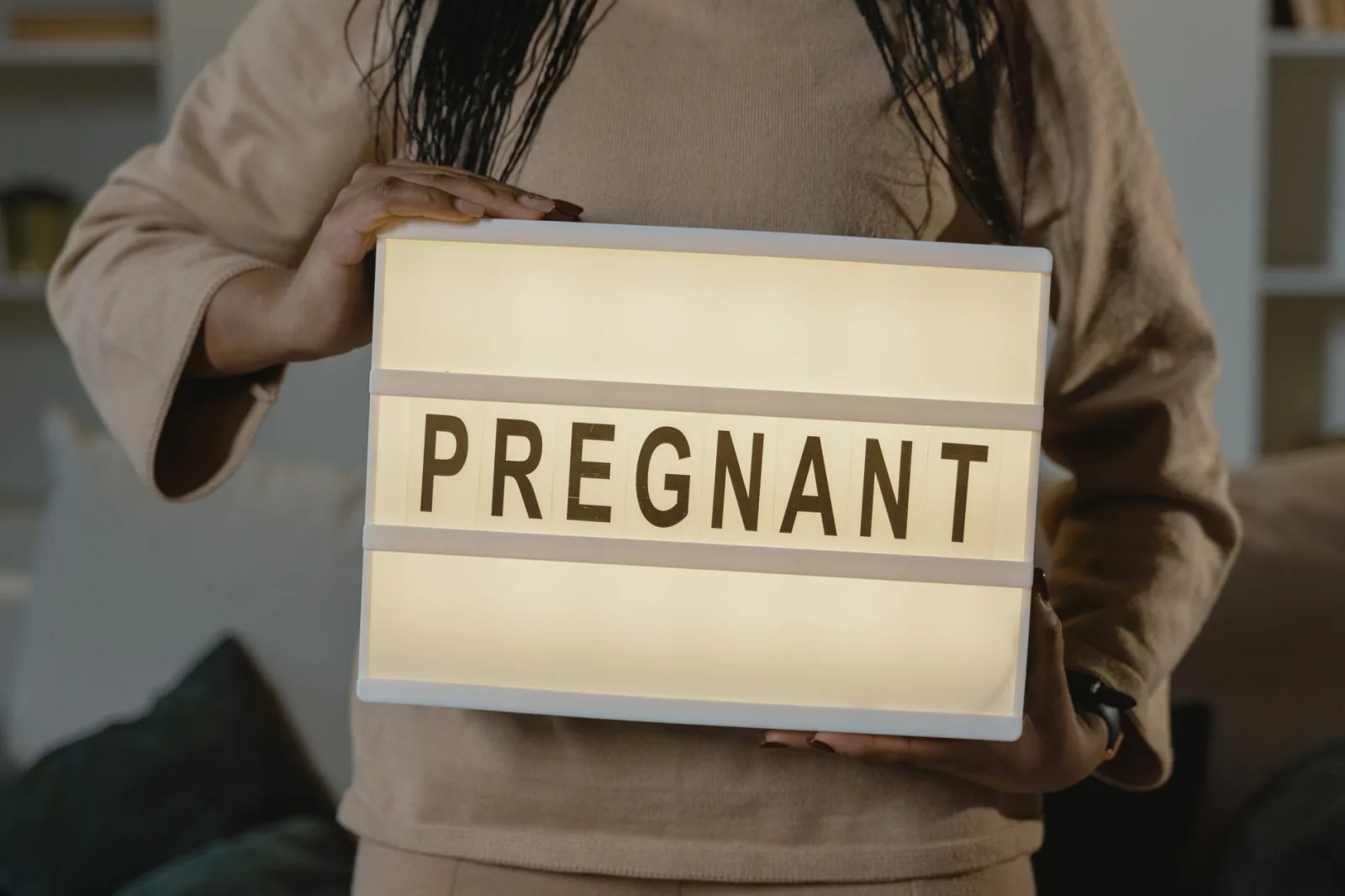 Woman displaying an illuminated 'PREGNANT' sign, symbolizing maternity and expectations.