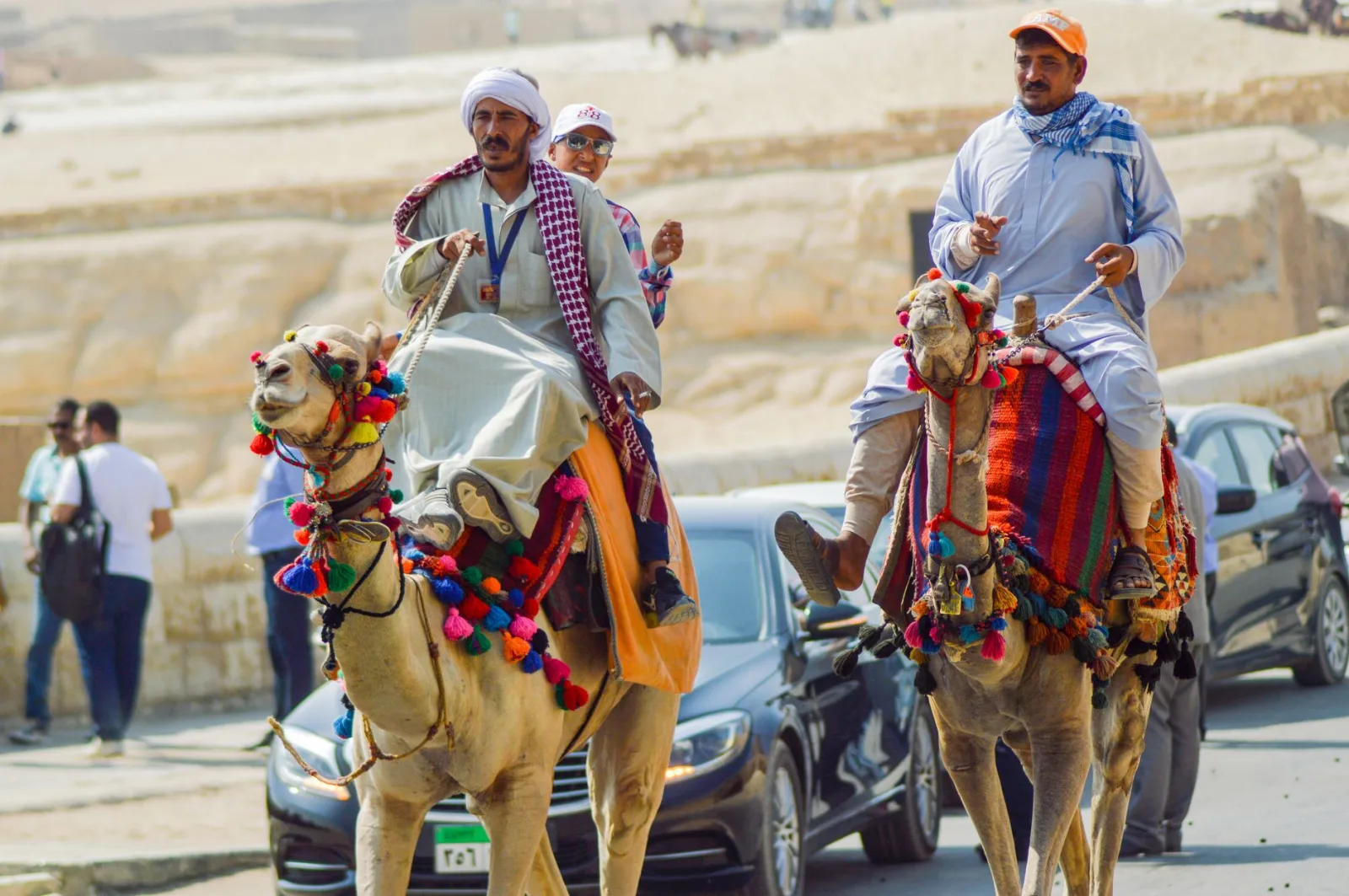 Camel riders in traditional attire explore the iconic Pyramids of Giza on a sunny day.