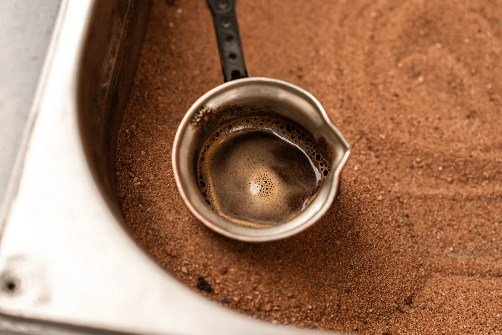A traditional Turkish coffee pot brewing in hot sand, showcasing an authentic Middle Eastern technique.