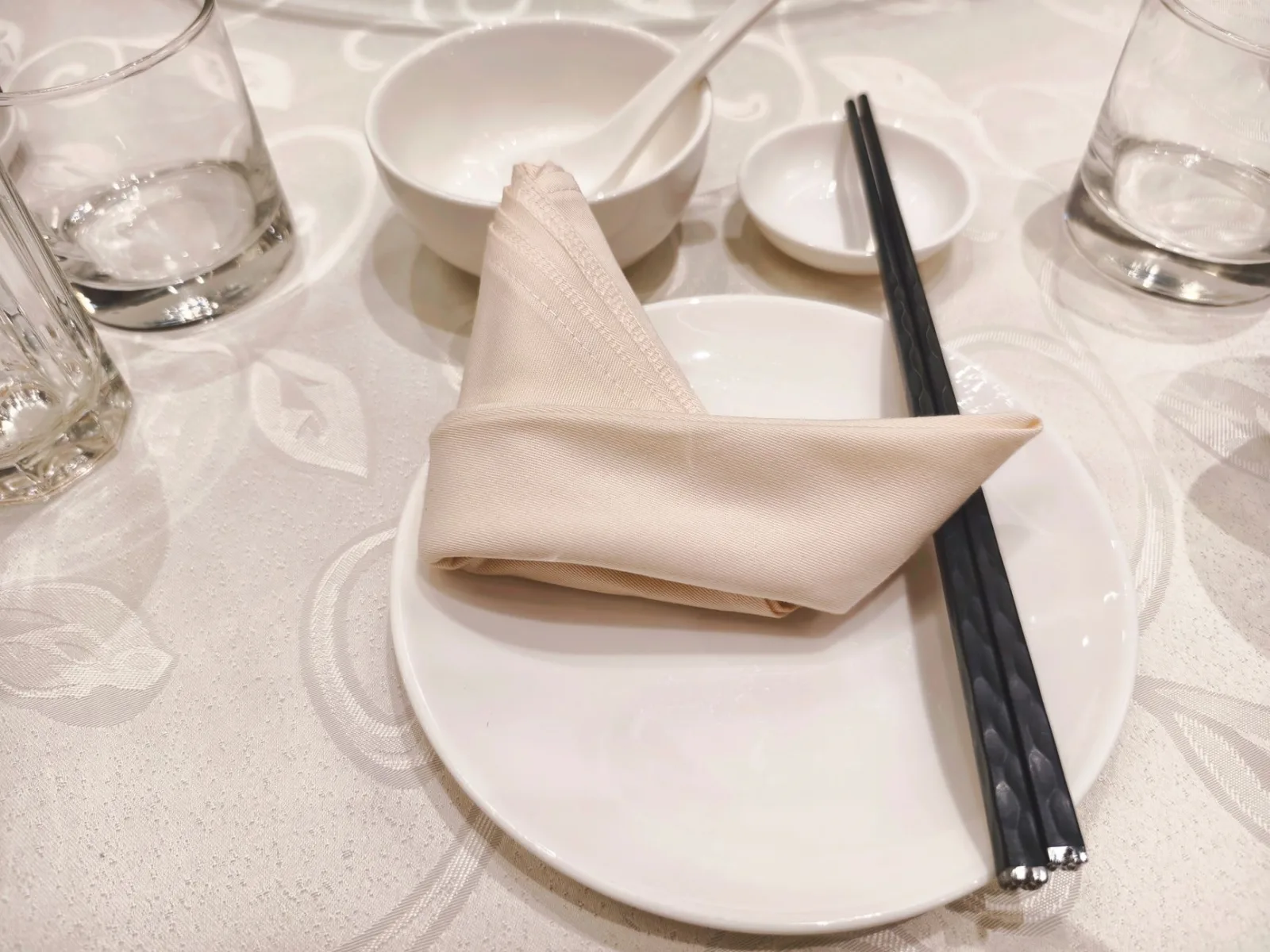 Minimalist table setting featuring a folded napkin, chopsticks, and glassware on a white tablecloth.