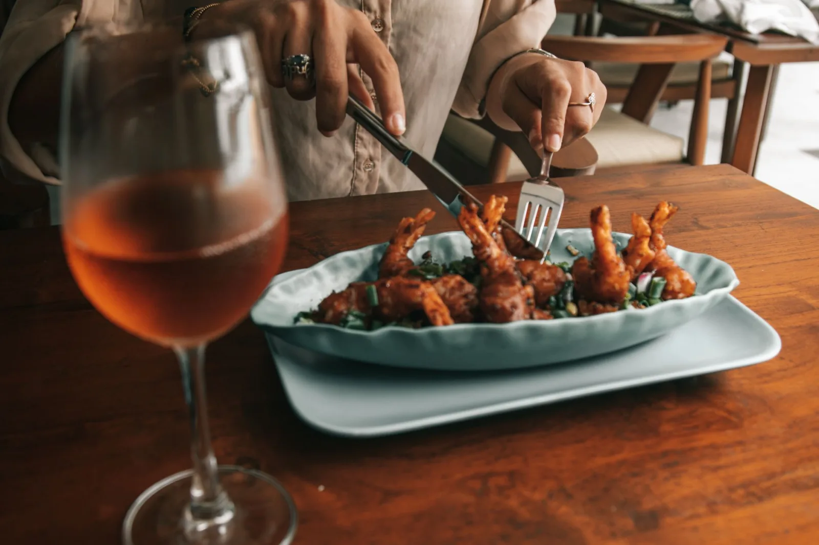 A person enjoys gourmet fried shrimp with a glass of rosé wine at an elegant dining setting.