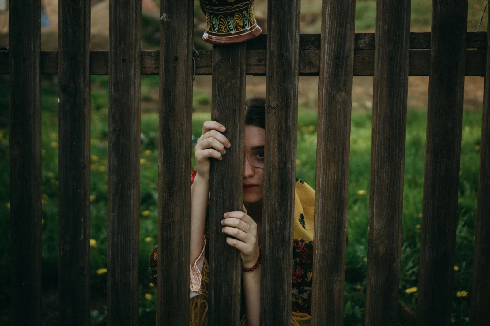 A woman peers through a wooden fence, creating a mysterious and intriguing scene.