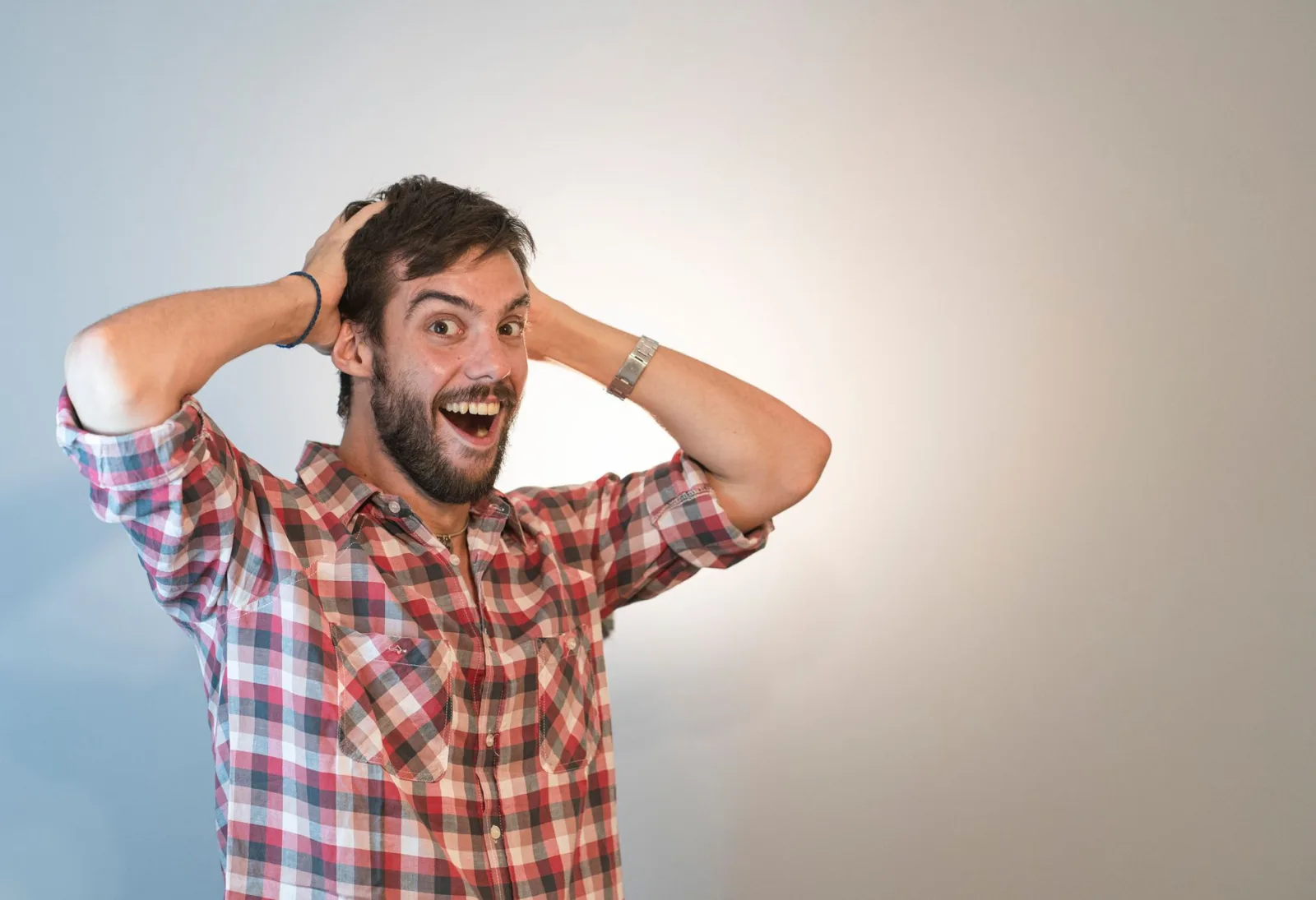 Surprised man with a beard in a red plaid shirt posing excitedly in a studio setting.