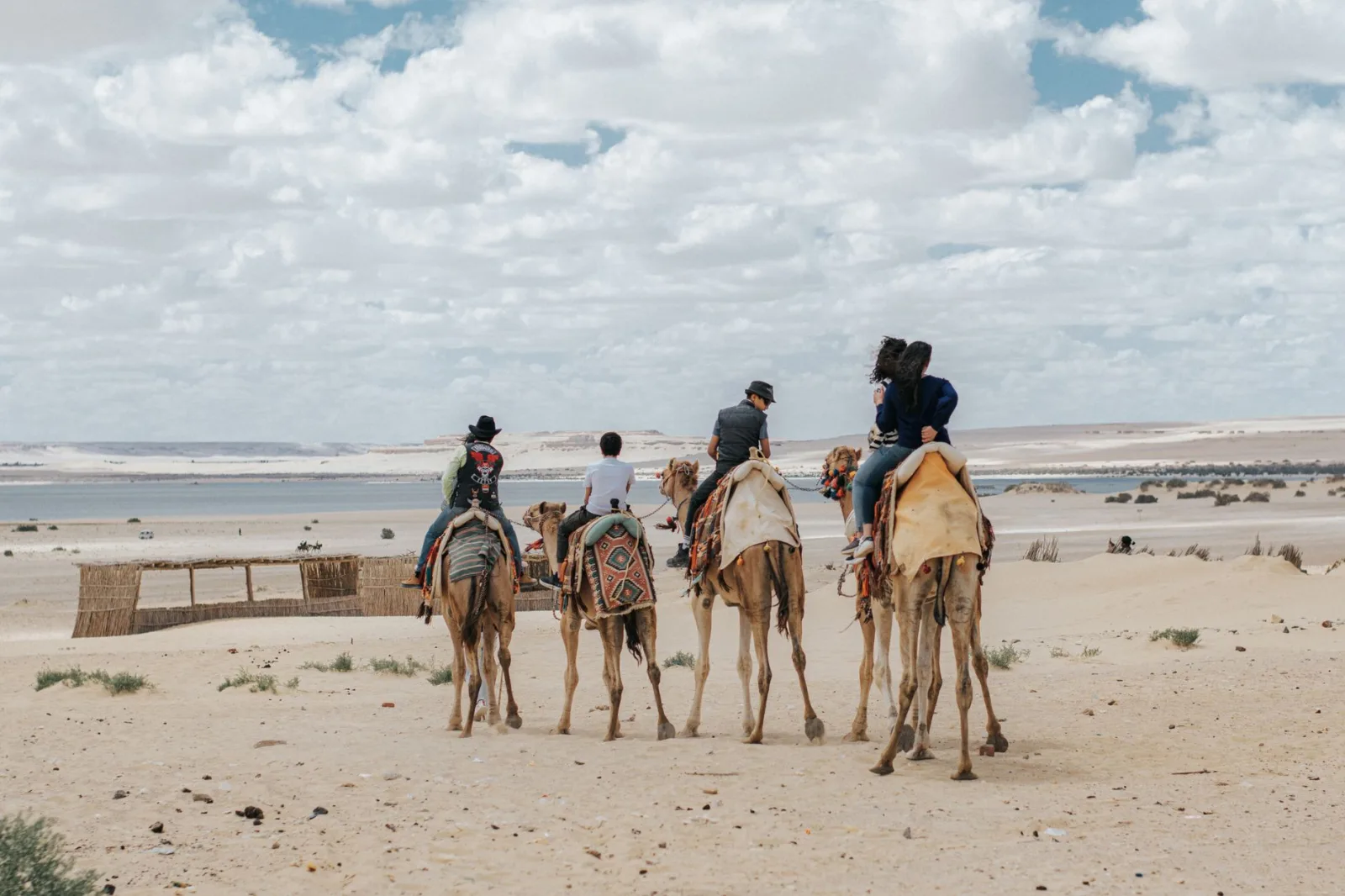 Group riding camels through Egypt's Faiyum desert, under a cloudy sky.