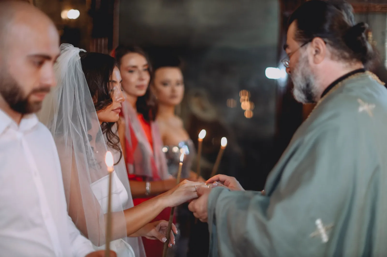 Couple exchanging rings at an Orthodox wedding ceremony with candles, focused priest.