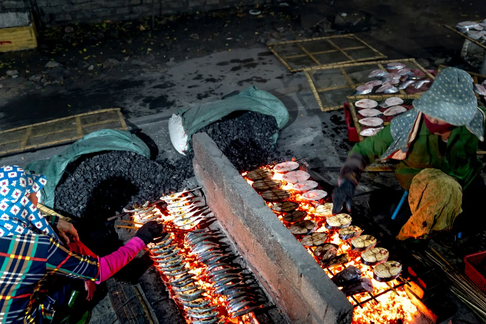 Vendors grilling fish over an open flame at an outdoor street market.