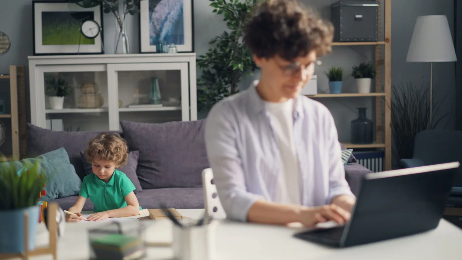 Mother Working on Laptop and Son Playing behind