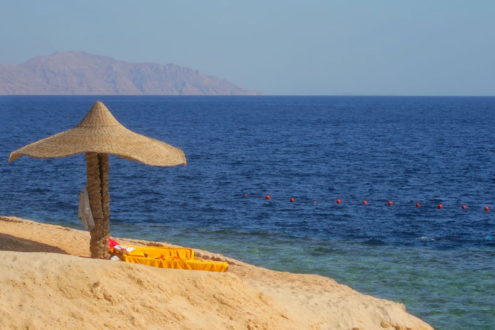 Serene beach with a straw parasol, sandy shore, and clear blue sea under a sunny sky.