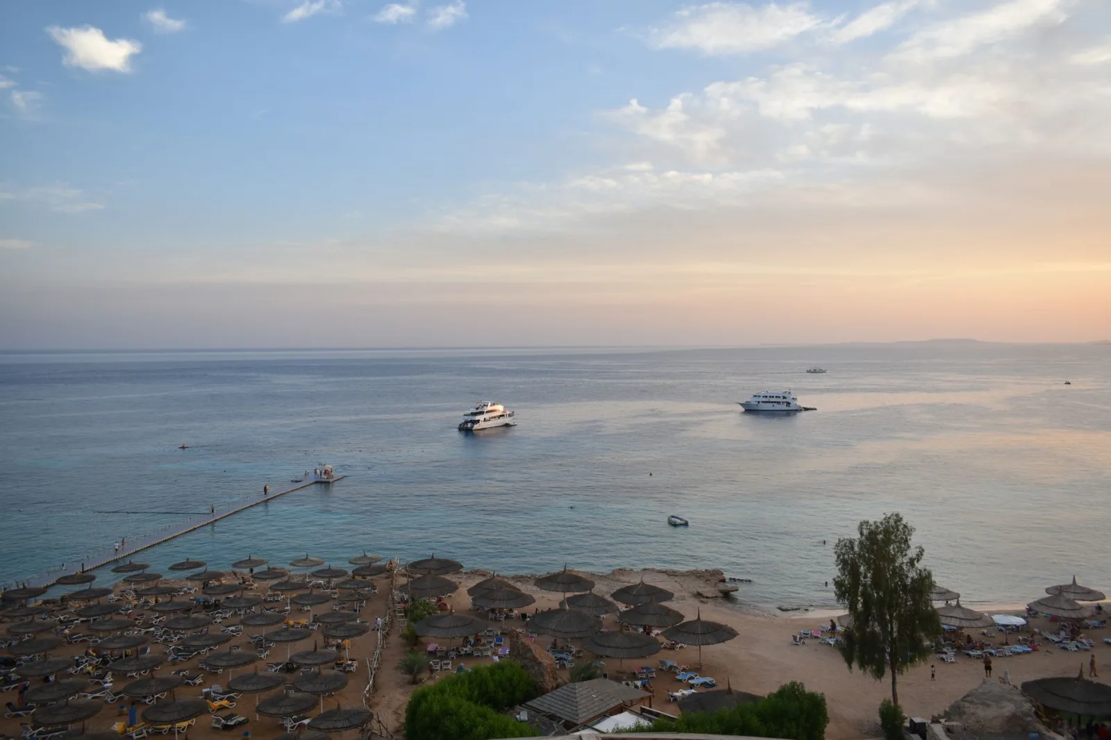Stunning aerial view of Sharm El Sheikh's beach and sea during sunset with boats and parasols.
