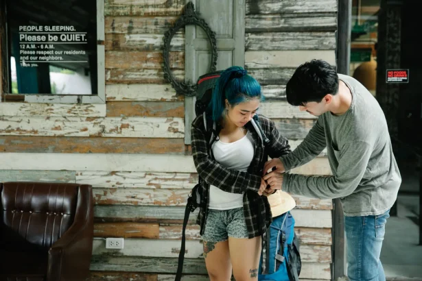 Two travelers prepare their backpacks in a rustic hostel lobby.