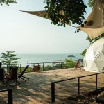 Relaxing outdoor deck with ocean view featuring a geodesic tent and deck chairs under shade.