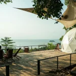 Relaxing outdoor deck with ocean view featuring a geodesic tent and deck chairs under shade.