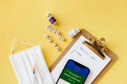 Flat lay of travel safety items: vaccine, mask, digital green pass on a vibrant yellow background.