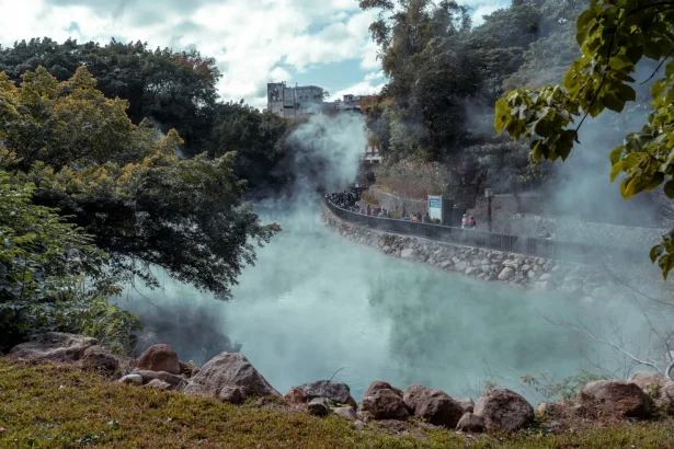 A serene hot spring landscape with steam rising amidst lush greenery, attracting tourists.