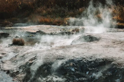 Hot soaring stream flowing over stones surrounded by hills with low grass at sunny day