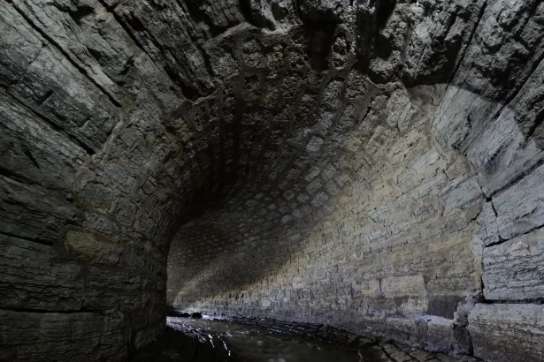 Atmospheric view of an old stone tunnel with a gentle stream flowing through it.