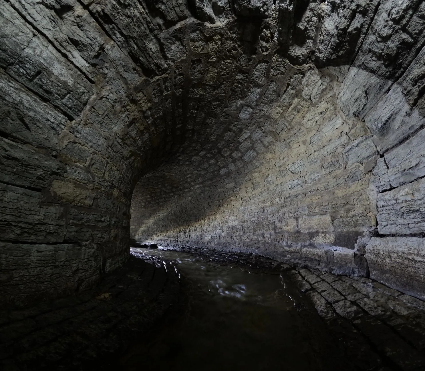 Atmospheric view of an old stone tunnel with a gentle stream flowing through it.