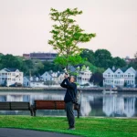 Photographer with long lens capturing nature in a serene suburban park by the water.