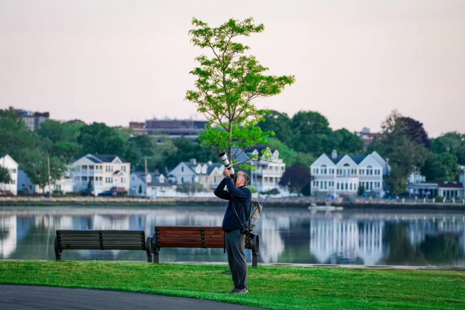 Photographer with long lens capturing nature in a serene suburban park by the water.