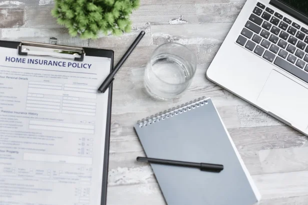 Flat lay of a workspace with a home insurance policy, laptop, and notebook on a desk.