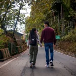 A couple holding hands, walking down a scenic forest road in autumn.