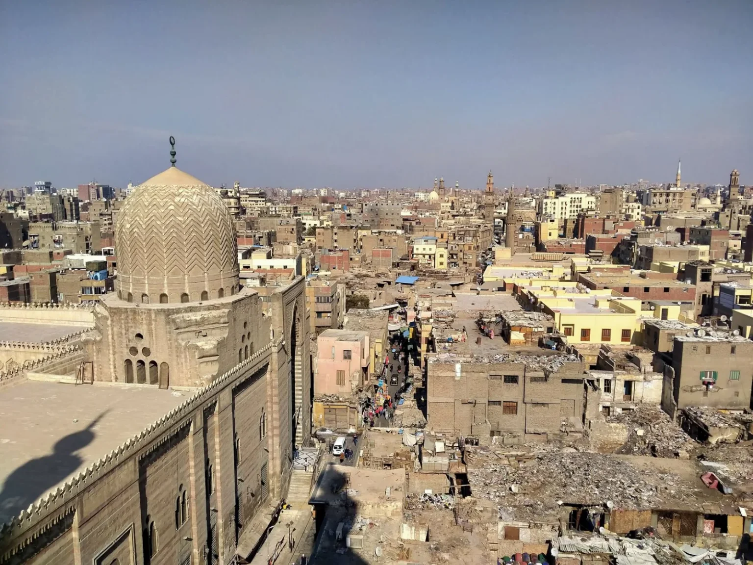 Aerial view of historic Old Cairo showcasing dense residential buildings and a prominent mosque dome under clear skies.