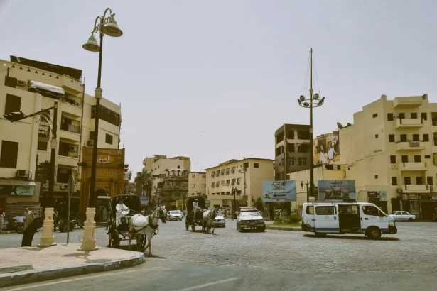 Busy intersection with horse-drawn carriages and vehicles in a Middle Eastern city.