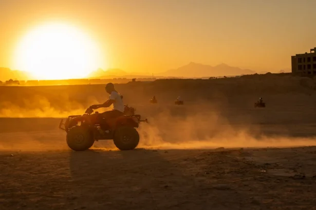 ATV riders explore the desert landscape at sunset, creating a scene filled with dust and motion.